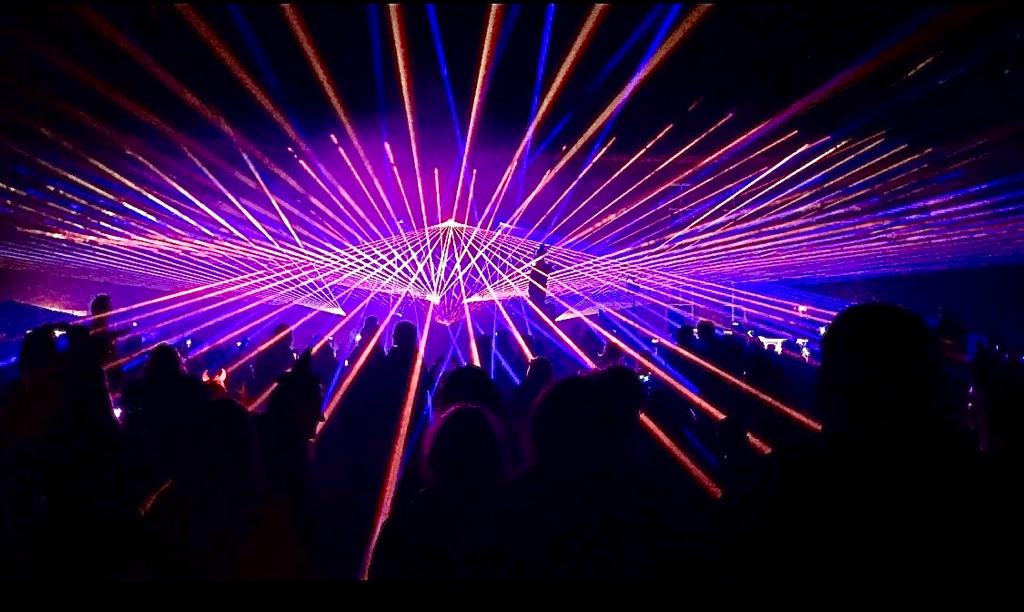 Lila Laserstrahlen in Sternform über dem Publikum einer Lasershow