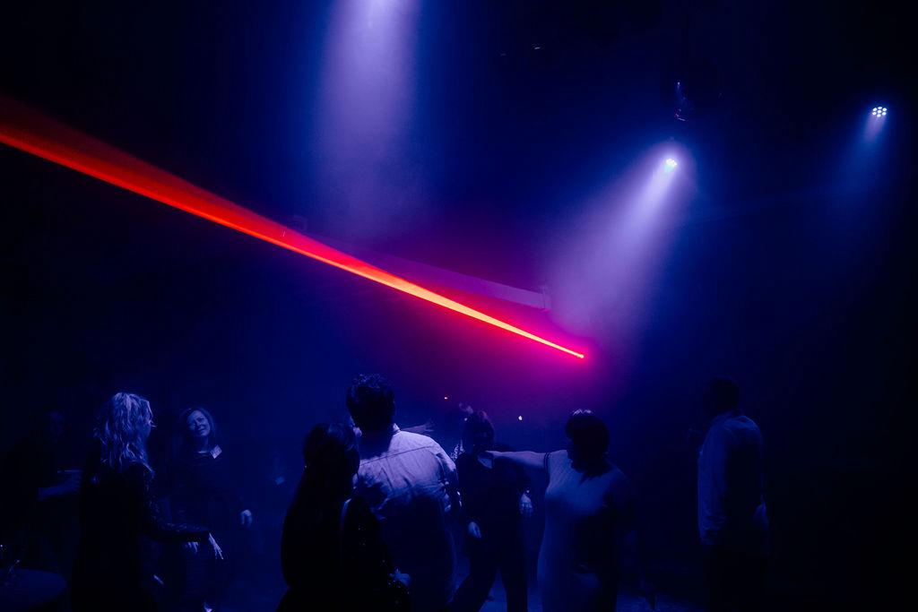 Dunkler Raum mit rotem Laserstrahl und blauem Scheinwerferlicht, Gäste tanzen